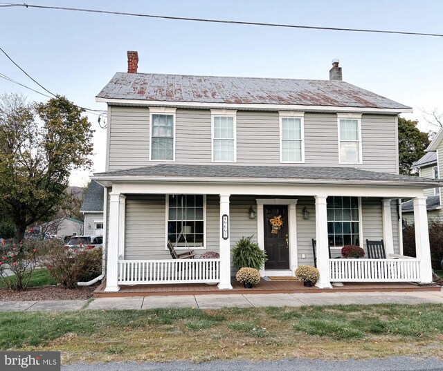 view of front facade featuring a chimney, metal roof, and a porch