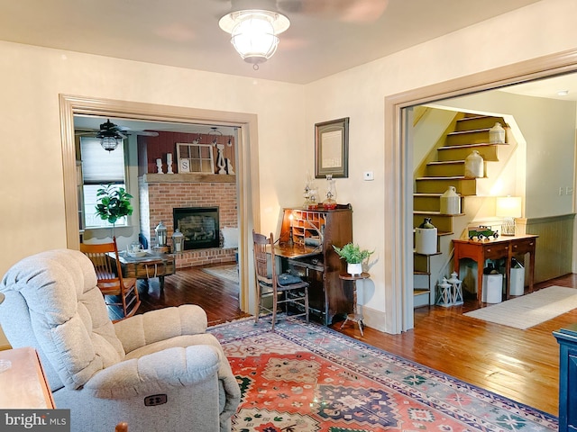 living room featuring hardwood / wood-style flooring, a ceiling fan, and a brick fireplace