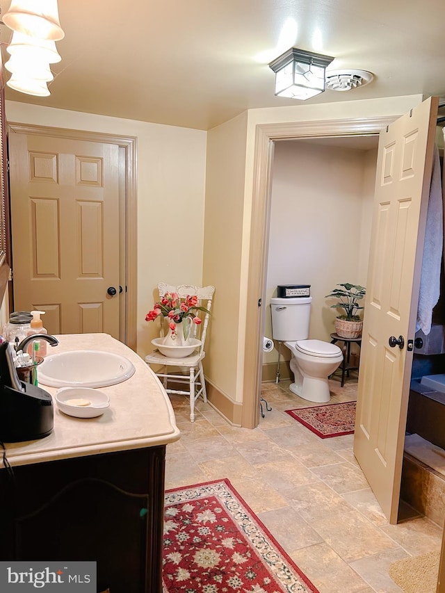 bathroom featuring baseboards, toilet, stone finish floor, and vanity