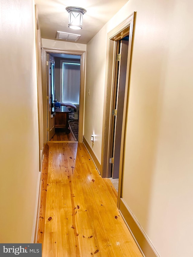corridor featuring baseboards, visible vents, attic access, and light wood-type flooring