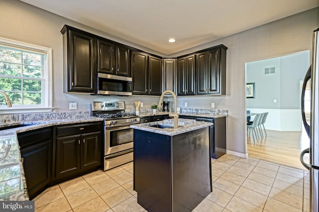 kitchen with a kitchen island, light stone countertops, sink, appliances with stainless steel finishes, and light tile patterned floors