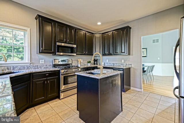 kitchen with visible vents, a kitchen island, appliances with stainless steel finishes, light stone counters, and a sink