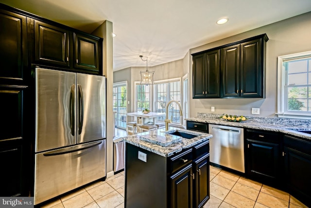 kitchen with a sink, appliances with stainless steel finishes, a center island with sink, light tile patterned flooring, and light stone counters