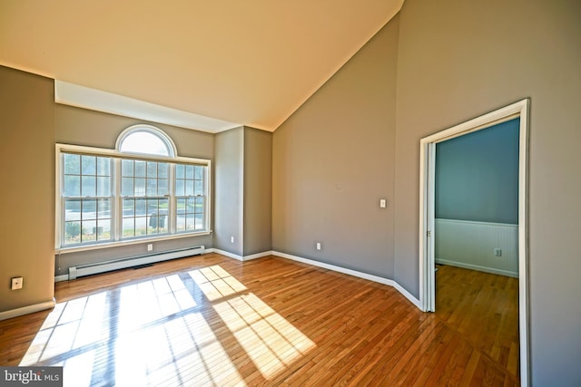 unfurnished room featuring a baseboard heating unit, wood finished floors, and lofted ceiling