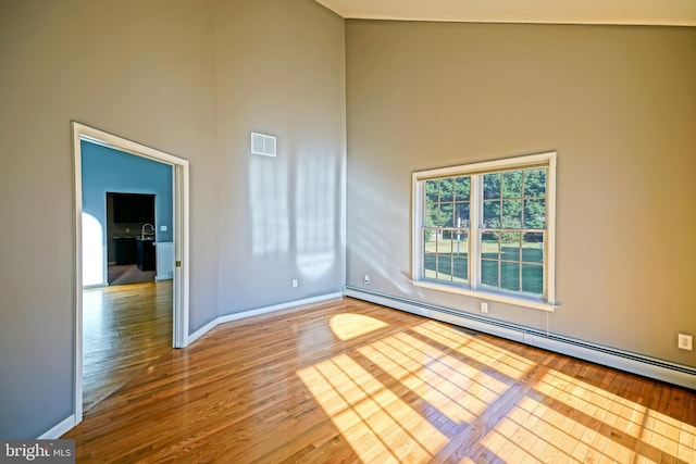 unfurnished room with a baseboard radiator, a high ceiling, wood finished floors, and visible vents