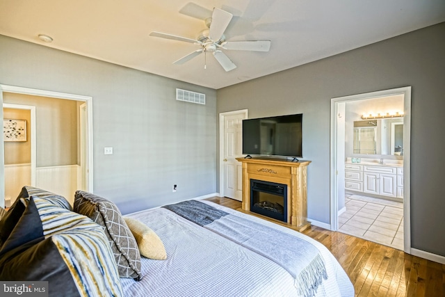 bedroom with visible vents, a ceiling fan, ensuite bath, hardwood / wood-style floors, and a glass covered fireplace