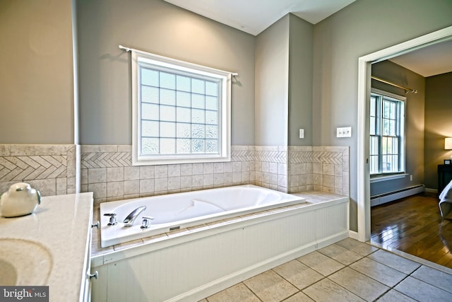 bathroom with plenty of natural light, hardwood / wood-style floors, a baseboard heating unit, and a tub to relax in