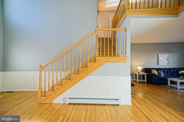 staircase with a towering ceiling, wood-type flooring, and baseboard heating