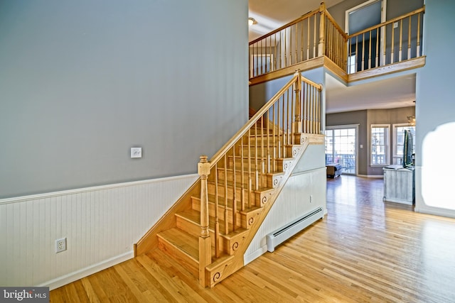 stairs with wood-type flooring, a towering ceiling, and a baseboard heating unit