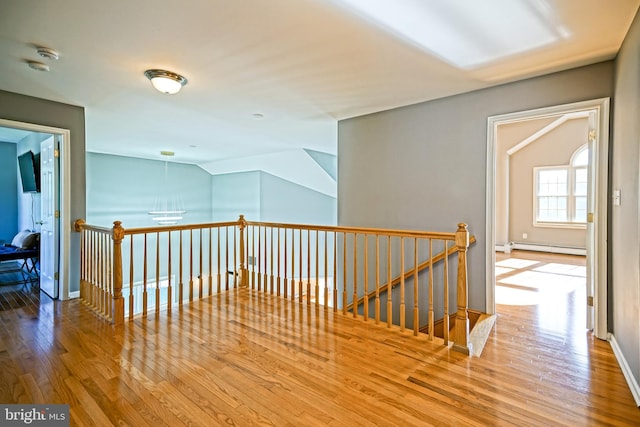 hallway with a baseboard radiator, wood finished floors, baseboards, and an upstairs landing