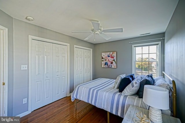 bedroom featuring dark hardwood / wood-style floors, multiple closets, and ceiling fan