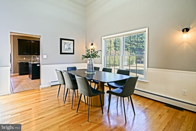 dining room featuring a towering ceiling, a baseboard radiator, sink, and light hardwood / wood-style floors