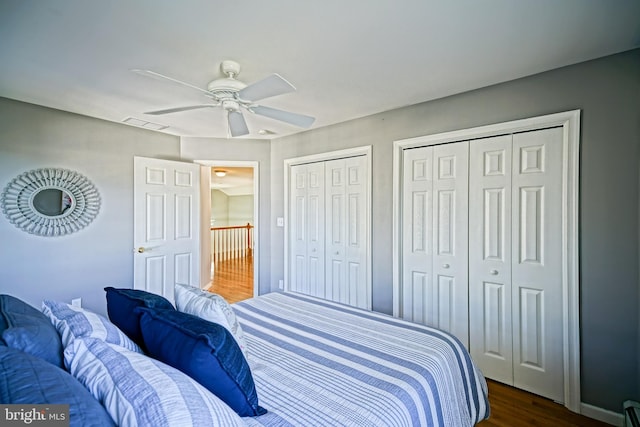bedroom featuring a baseboard heating unit, dark wood-style floors, two closets, a ceiling fan, and visible vents