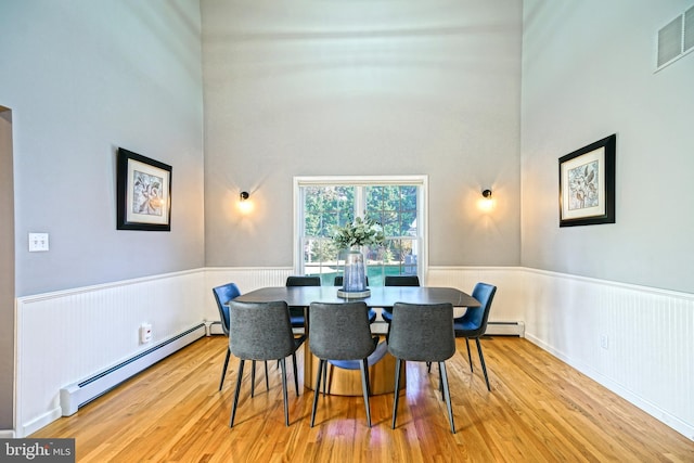 dining room with visible vents, a baseboard heating unit, a wainscoted wall, and wood finished floors