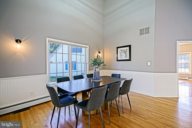 dining area with light hardwood / wood-style flooring, a high ceiling, and a baseboard heating unit