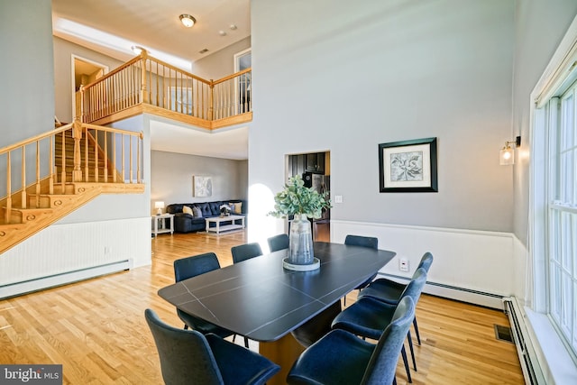 dining area featuring a baseboard radiator, stairway, a high ceiling, and wood finished floors
