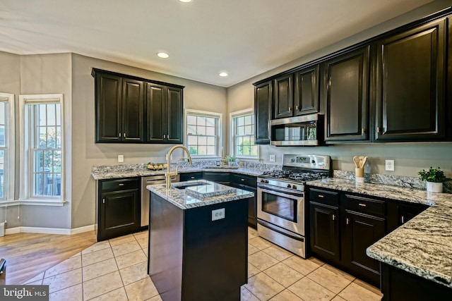 kitchen featuring light stone counters, recessed lighting, a kitchen island with sink, dark cabinetry, and stainless steel appliances