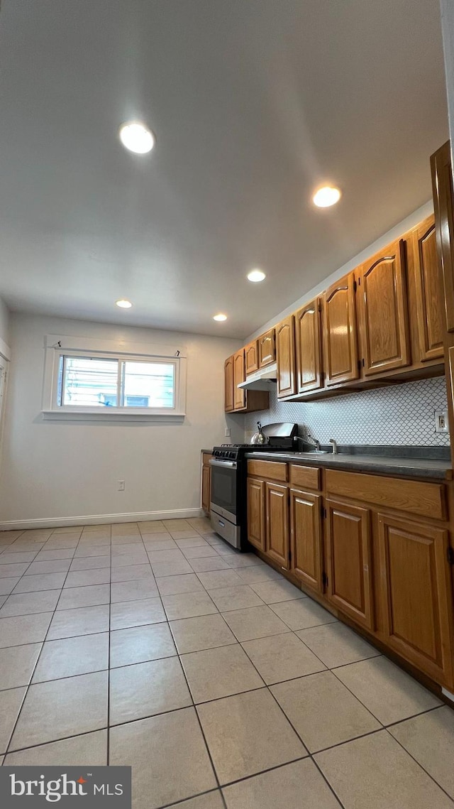 kitchen featuring light tile patterned flooring, backsplash, and stainless steel range with gas cooktop