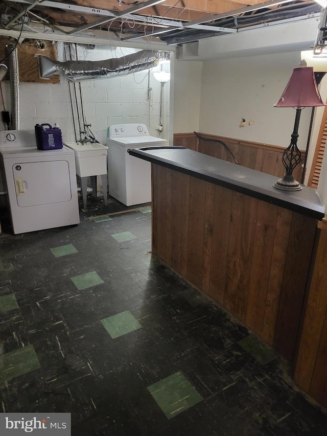 unfinished below grade area with dark floors, concrete block wall, a wainscoted wall, washer and clothes dryer, and a sink