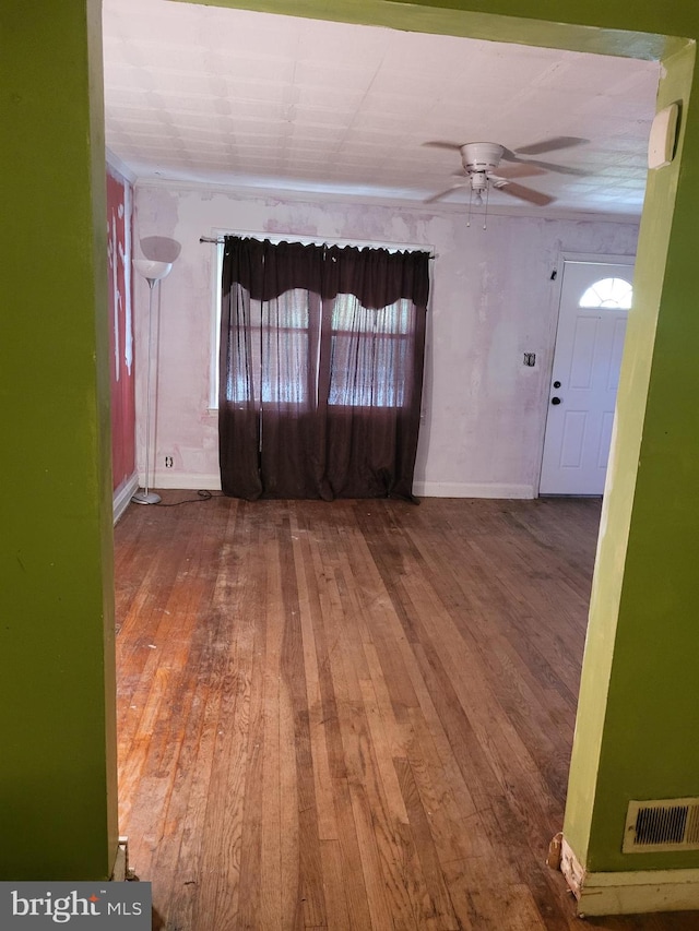 unfurnished room with ceiling fan, wood-type flooring, visible vents, and baseboards