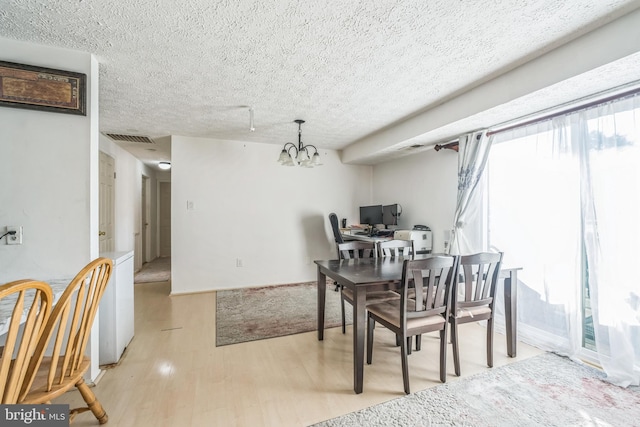 dining room with an inviting chandelier, a textured ceiling, and light wood-type flooring