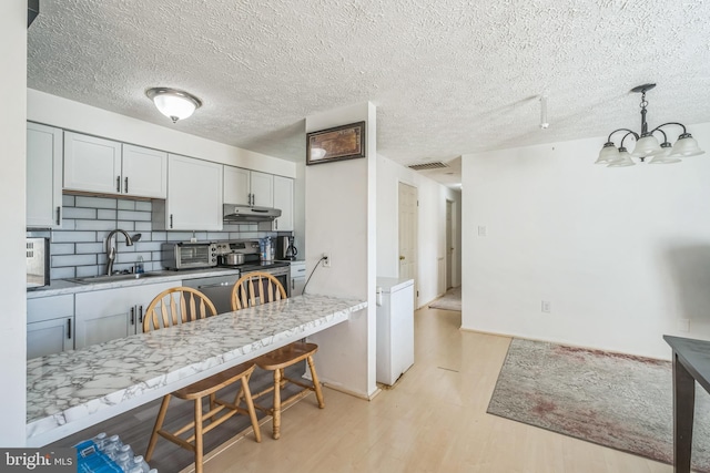 kitchen featuring backsplash, appliances with stainless steel finishes, light wood-type flooring, sink, and decorative light fixtures