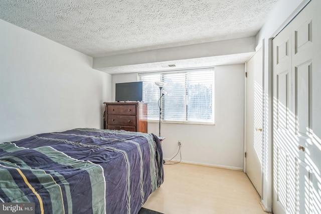 bedroom with a closet, a textured ceiling, and light hardwood / wood-style flooring