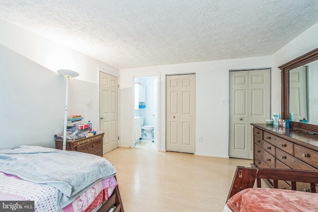 bedroom featuring a textured ceiling, ensuite bathroom, and multiple closets