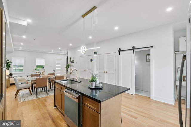 kitchen with light wood-type flooring, a barn door, a center island with sink, and hanging light fixtures