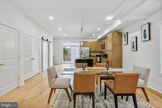 dining space with a barn door and light hardwood / wood-style floors