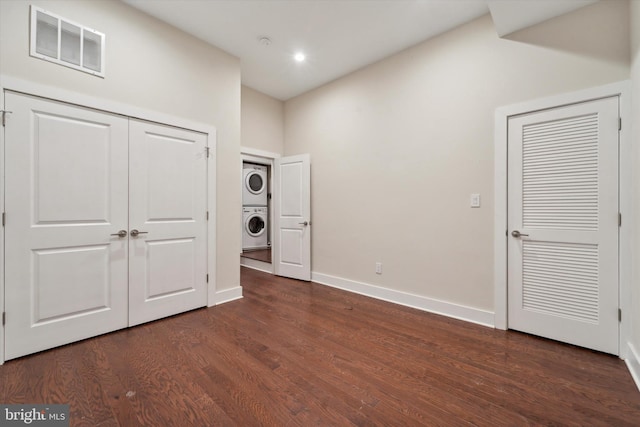 unfurnished bedroom featuring stacked washer and dryer and dark hardwood / wood-style flooring