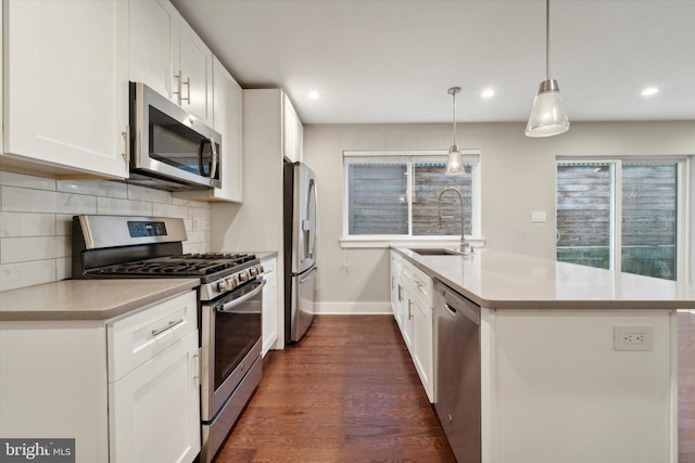 kitchen with appliances with stainless steel finishes, sink, hanging light fixtures, white cabinetry, and dark wood-type flooring