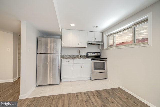 kitchen with white cabinets, appliances with stainless steel finishes, sink, light hardwood / wood-style floors, and light stone counters