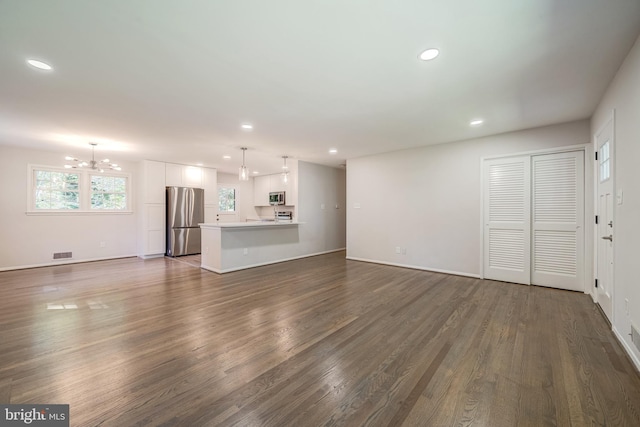 unfurnished living room featuring an inviting chandelier and dark hardwood / wood-style flooring