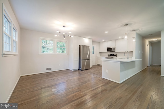 kitchen with dark wood-type flooring, kitchen peninsula, pendant lighting, white cabinetry, and appliances with stainless steel finishes