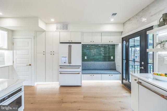 kitchen with white cabinetry, light stone countertops, high end white fridge, and light hardwood / wood-style floors