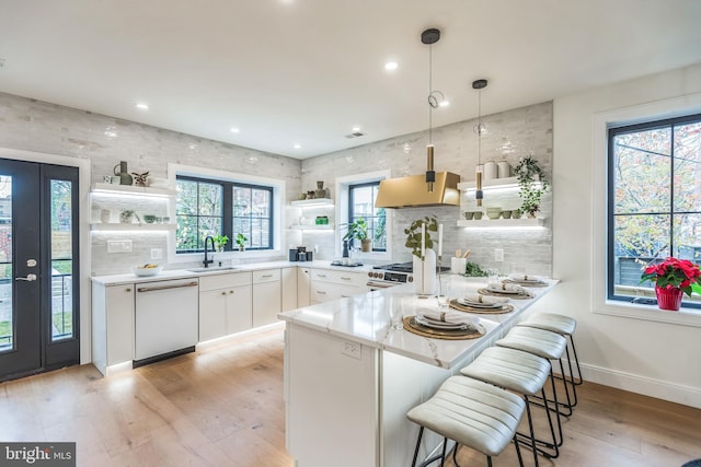 kitchen featuring a breakfast bar area, white cabinetry, white dishwasher, decorative light fixtures, and kitchen peninsula