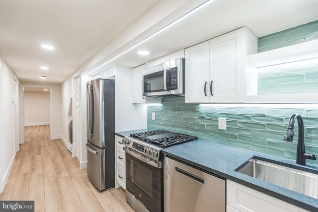 kitchen featuring white cabinetry, sink, backsplash, light hardwood / wood-style floors, and stainless steel appliances