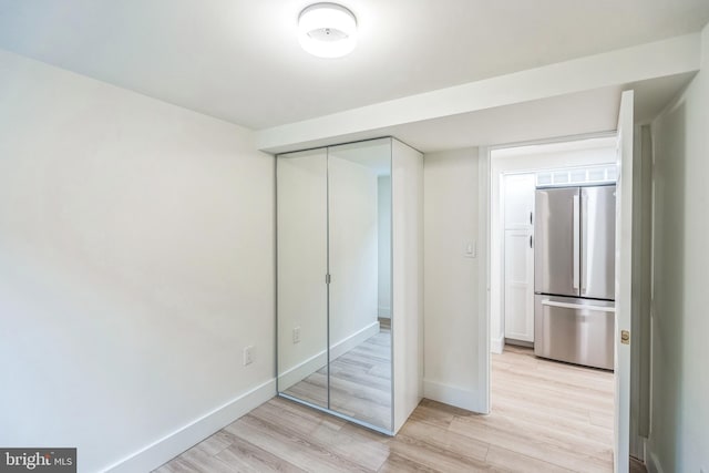 unfurnished bedroom featuring stainless steel fridge, a closet, and light wood-type flooring