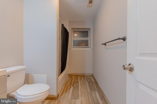 bathroom with hardwood / wood-style flooring, shower / bath combo with shower curtain, and toilet