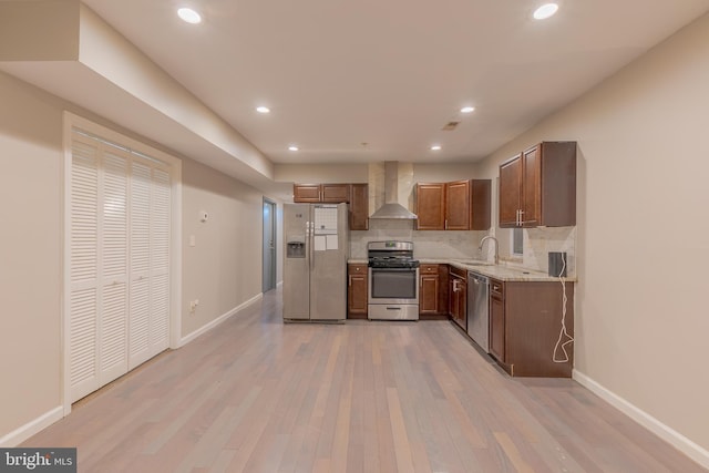 kitchen featuring wall chimney exhaust hood, light hardwood / wood-style flooring, sink, backsplash, and appliances with stainless steel finishes