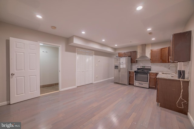 kitchen featuring wall chimney exhaust hood, white fridge with ice dispenser, sink, light hardwood / wood-style floors, and stainless steel gas range oven