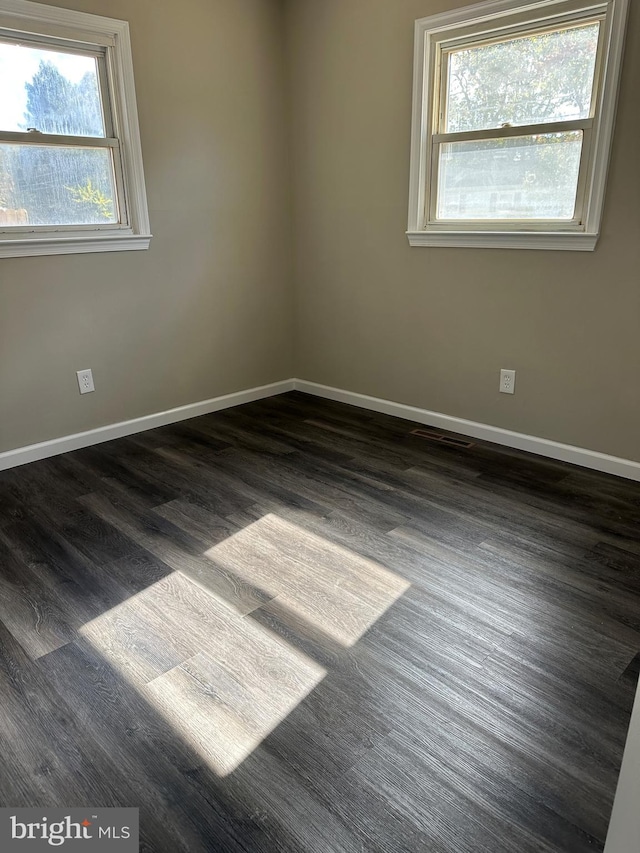 empty room featuring dark wood-type flooring and a healthy amount of sunlight