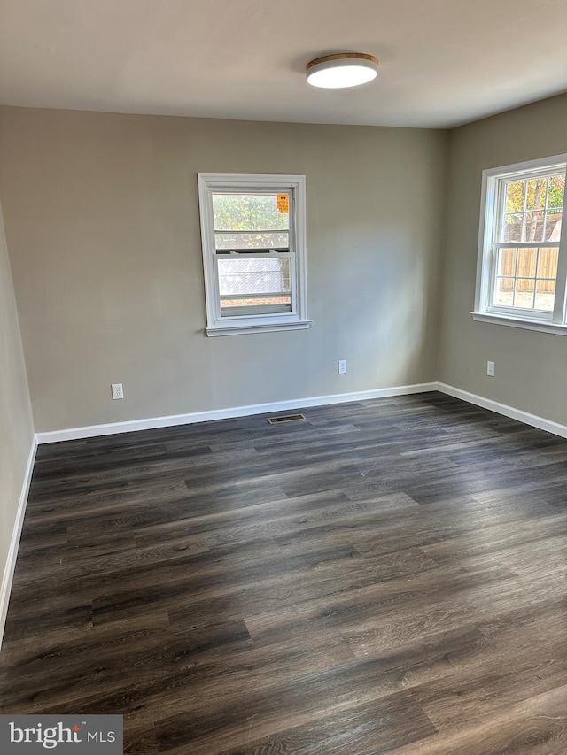 unfurnished room featuring baseboards, dark wood-style floors, and visible vents