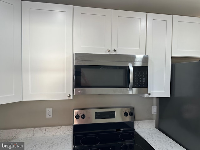 kitchen featuring white cabinetry, light stone counters, and range with electric stovetop