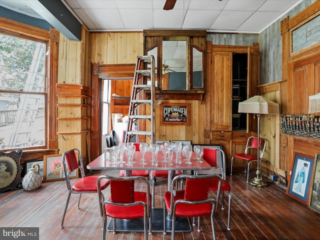 dining area featuring dark hardwood / wood-style flooring, a drop ceiling, and wood walls