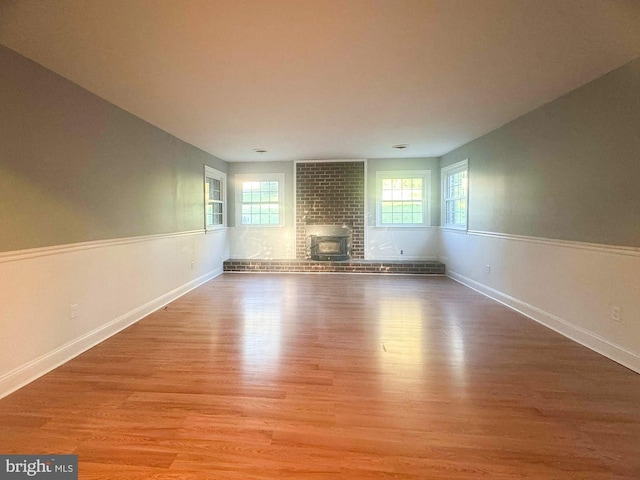 unfurnished living room featuring a healthy amount of sunlight, a wood stove, and light wood-type flooring