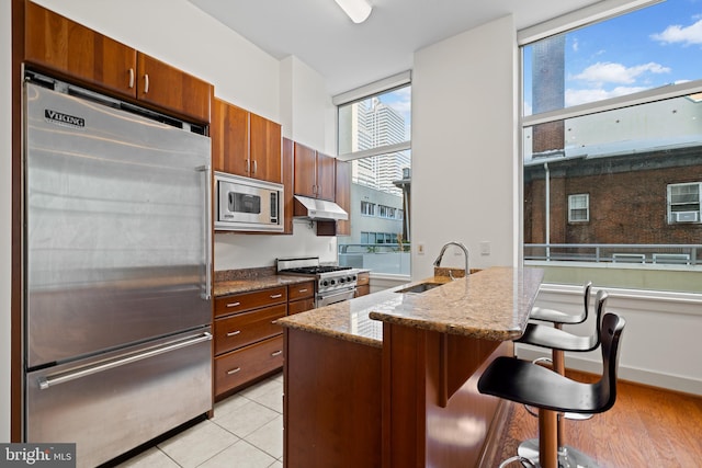 kitchen with high quality appliances, sink, a kitchen bar, light stone counters, and light hardwood / wood-style floors