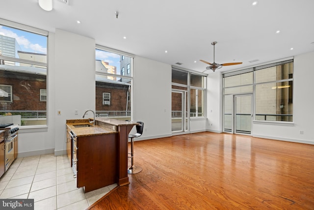 kitchen featuring light stone countertops, sink, a kitchen breakfast bar, high end stove, and light hardwood / wood-style flooring