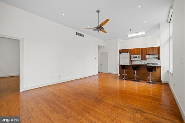 unfurnished living room with ceiling fan, sink, light wood-type flooring, and a high ceiling